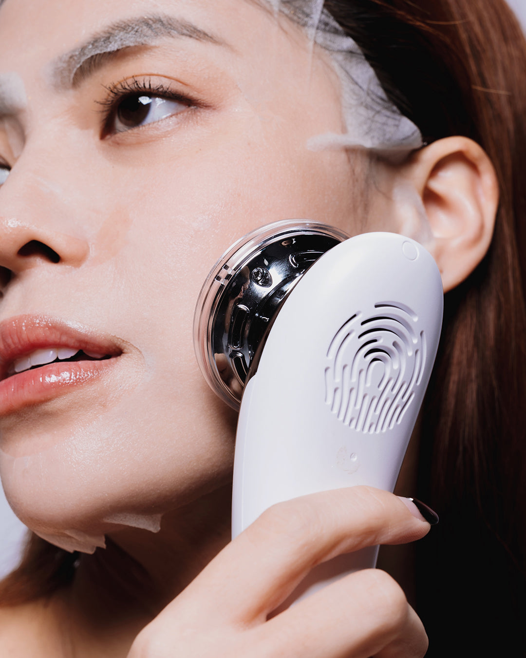 Woman using BRIXX DERMA electronic device on their face against a dark background