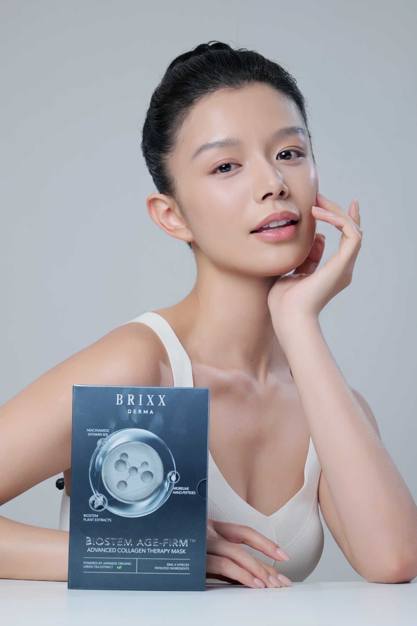 Woman holding a Brixx Derma skincare product box against a plain background